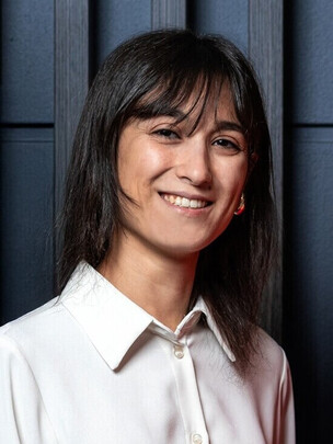 Porträt von Francesca Paoletti vor dunklem Hintergrund, sie trägt eine weiße Bluse und lächelt.